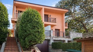 A modern two-story building with a staircase leading to the entrance, surrounded by greenery and a stone wall. - Vivienda Vacacional Eltxok (Llanes)