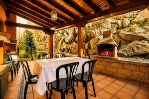 Une terrasse extérieure avec un mur en pierre, un four en briques et une table dressée pour le repas.