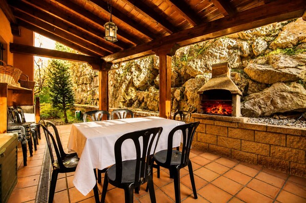 An outdoor patio with a stone wall, a brick oven, and a table set for dining.