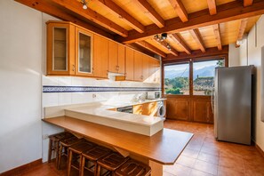 A kitchen with wooden cabinets, a stainless steel refrigerator, a washing machine, and a large window with a view of mountains. - Casa la Encina de Pancar (Pancar)