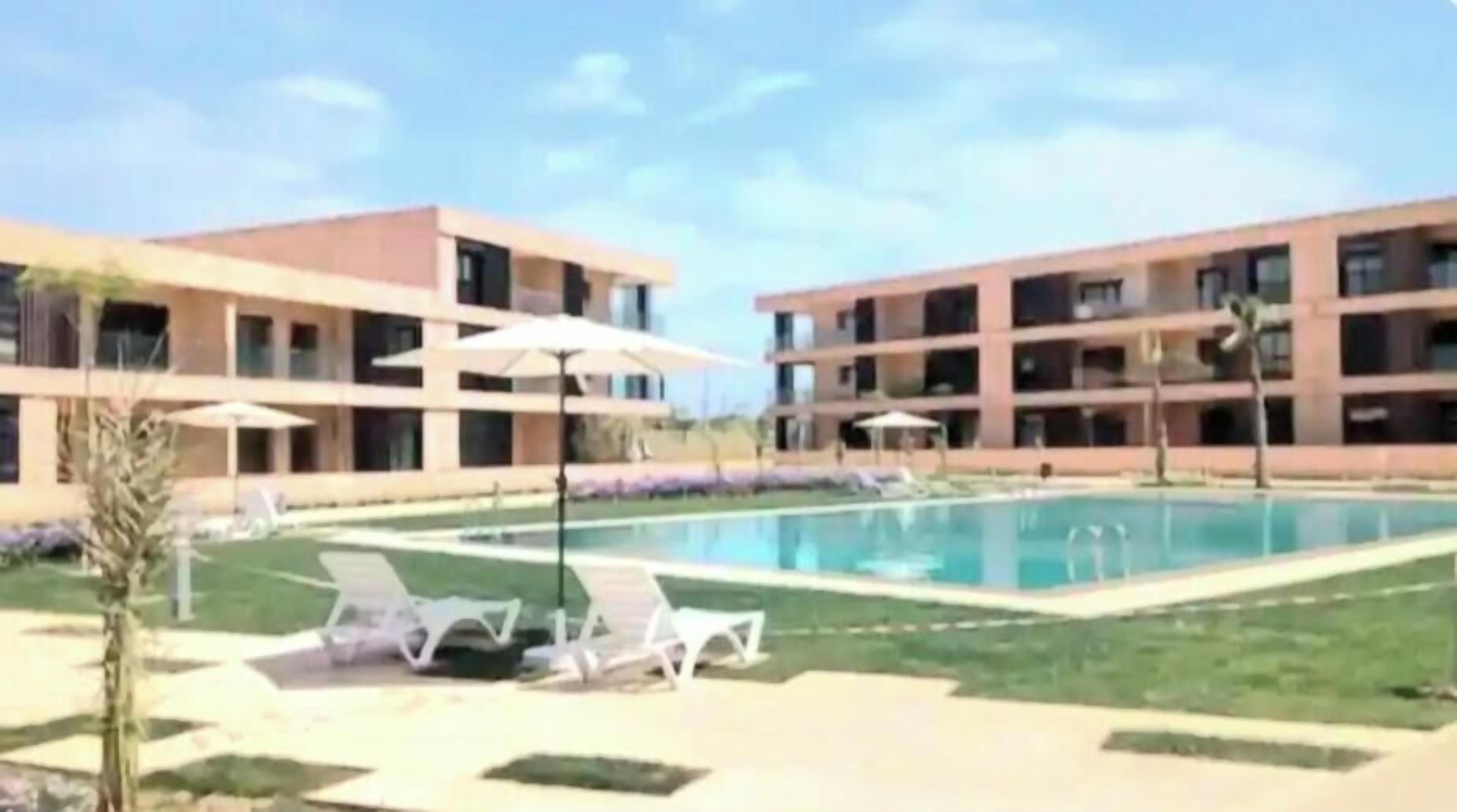 A modern building with a swimming pool, lounge chairs, and umbrellas.