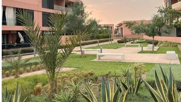 A modern building with a flat roof and large windows, surrounded by a well-maintained garden with various plants and a paved walkway. - Appartement Sympa (Marrakech)