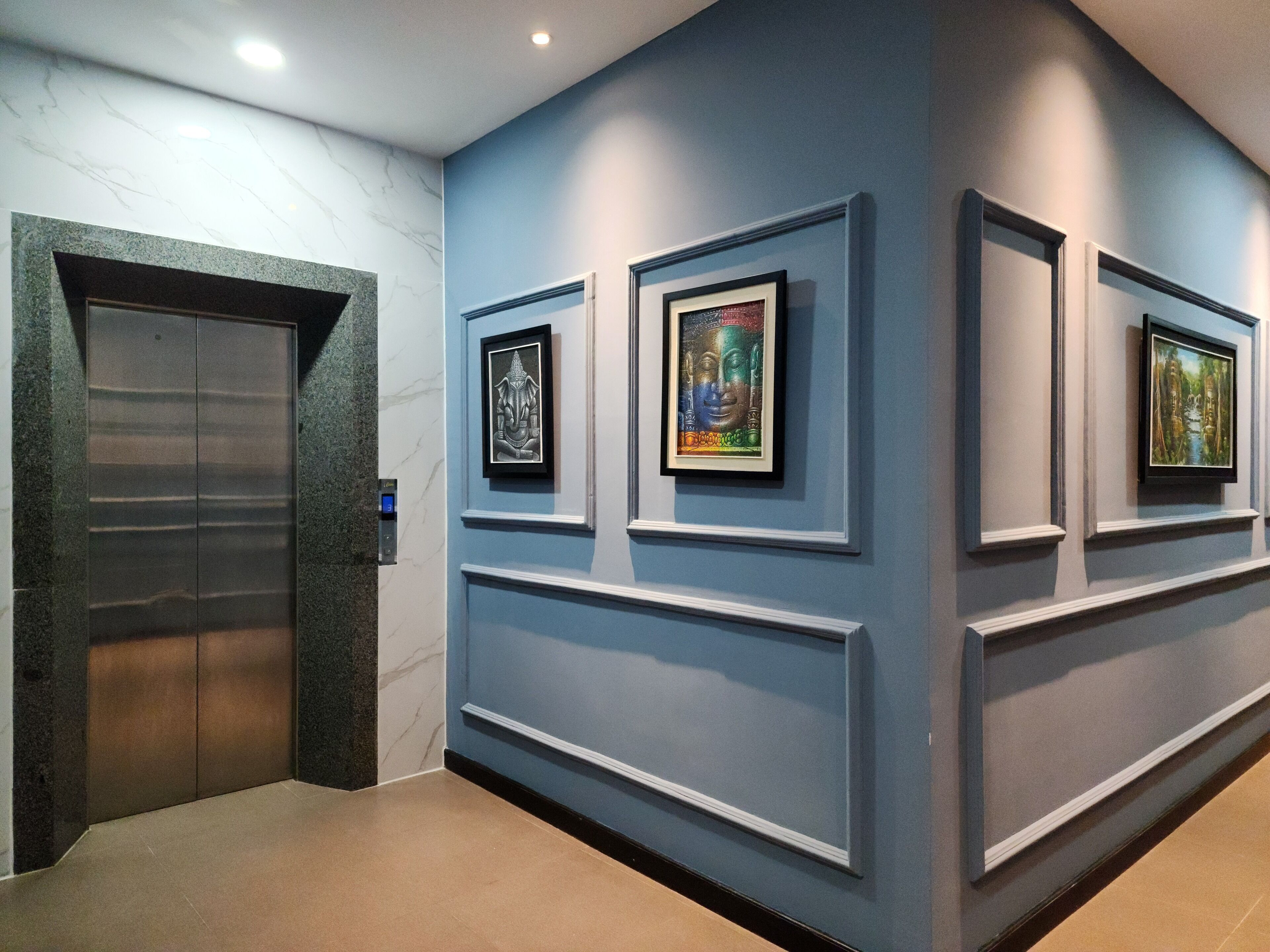 Un couloir avec un mur en marbre, un ascenseur et des œuvres d’art encadrées accrochées au mur.