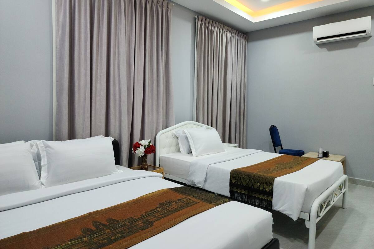 A hotel room with two beds, a small table, a chair, and an air conditioning unit.