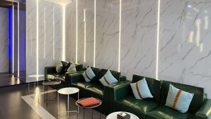 A modern lobby with a green sofa set, white marble walls, and a sleek ceiling design.