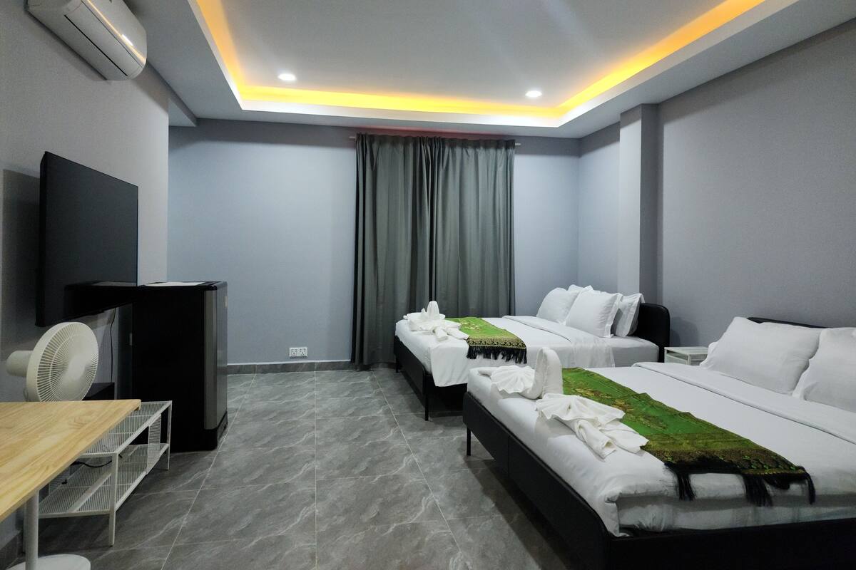 A hotel room with two beds, a TV, a fan, and a desk.
