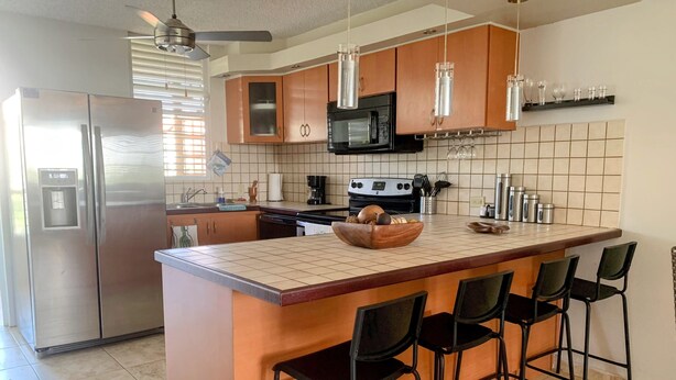 A modern kitchen with a central island, stainless steel appliances, and black bar stools. - Spacious 3 bedrooms penthouse, near Combate Beach: Pools, Fun & Amazing Sunsets (Cabo Rojo)