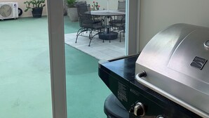 A patio area with a grill, a table with chairs, and a potted plant. - Spacious 3 bedrooms penthouse, near Combate Beach: Pools, Fun & Amazing Sunsets (Cabo Rojo)