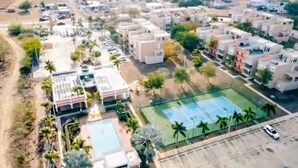 An aerial view of a residential area with modern buildings, a tennis court, and a parking lot. - Spacious 3 bedrooms penthouse, near Combate Beach: Pools, Fun & Amazing Sunsets (Cabo Rojo)