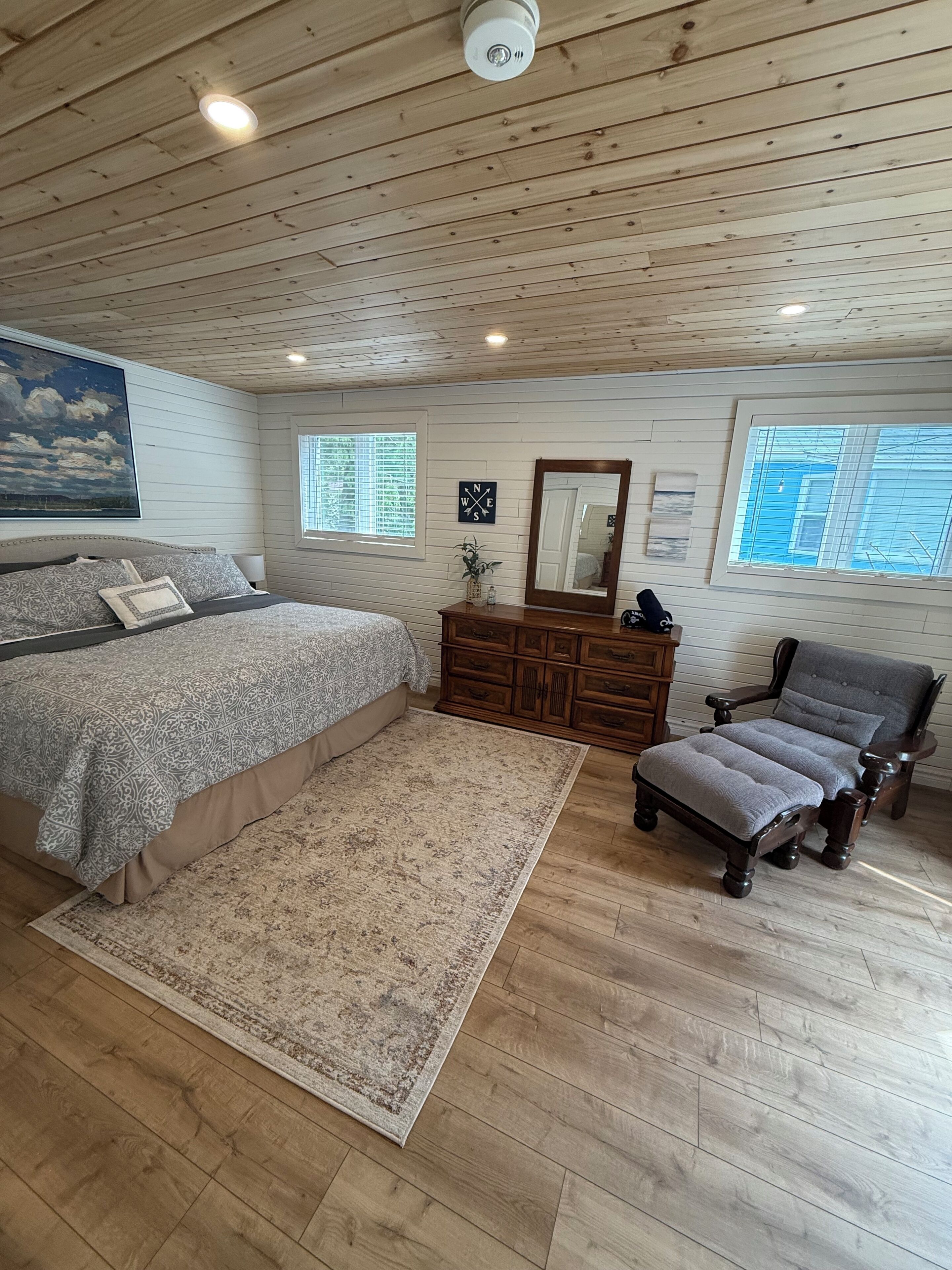 A bedroom with a bed, dresser, chair, and a large painting on the wall.