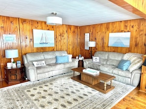 A living room with two sofas, a coffee table, a rug, and wooden walls with framed pictures.