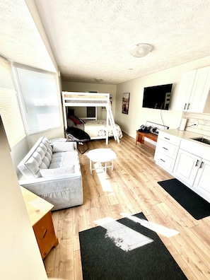 A compact living space with a bunk bed, sofa, dining table, kitchen area, and a TV.