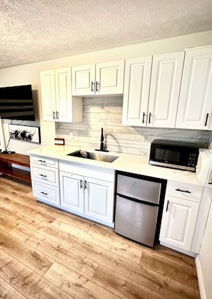 A kitchen with white cabinets, a stainless steel dishwasher, a microwave, and a wooden floor.