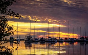 A marina with multiple sailboats docked, surrounded by calm water reflecting the sunset.