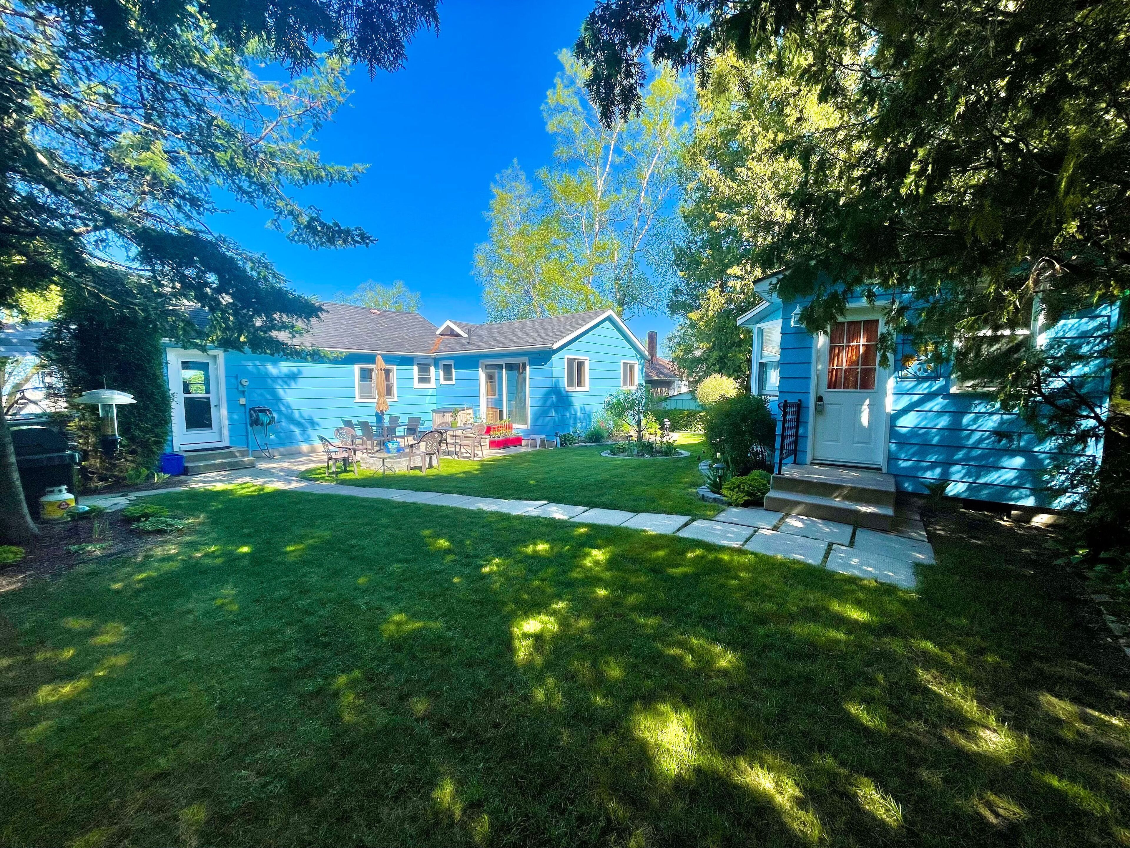 A blue house with a front yard, a patio with chairs, and a small garden.