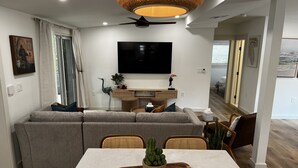 Een moderne woonkamer met een bank, een eettafel en een flatscreen televisie aan de muur.