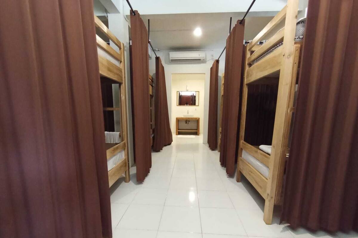 Un pasillo con literas y cortinas que conduce a un baño con lavabo y espejo.