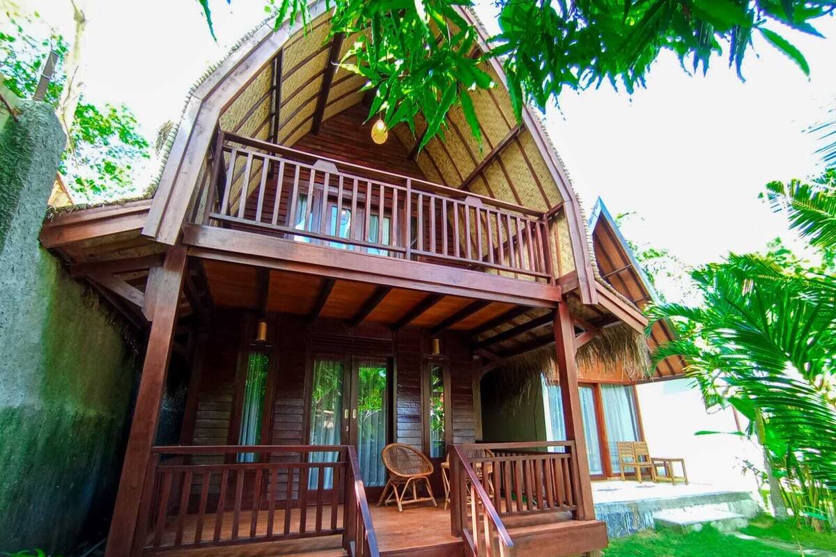 Una casa de madera con balcón, porche y un pequeño espacio exterior con mobiliario.