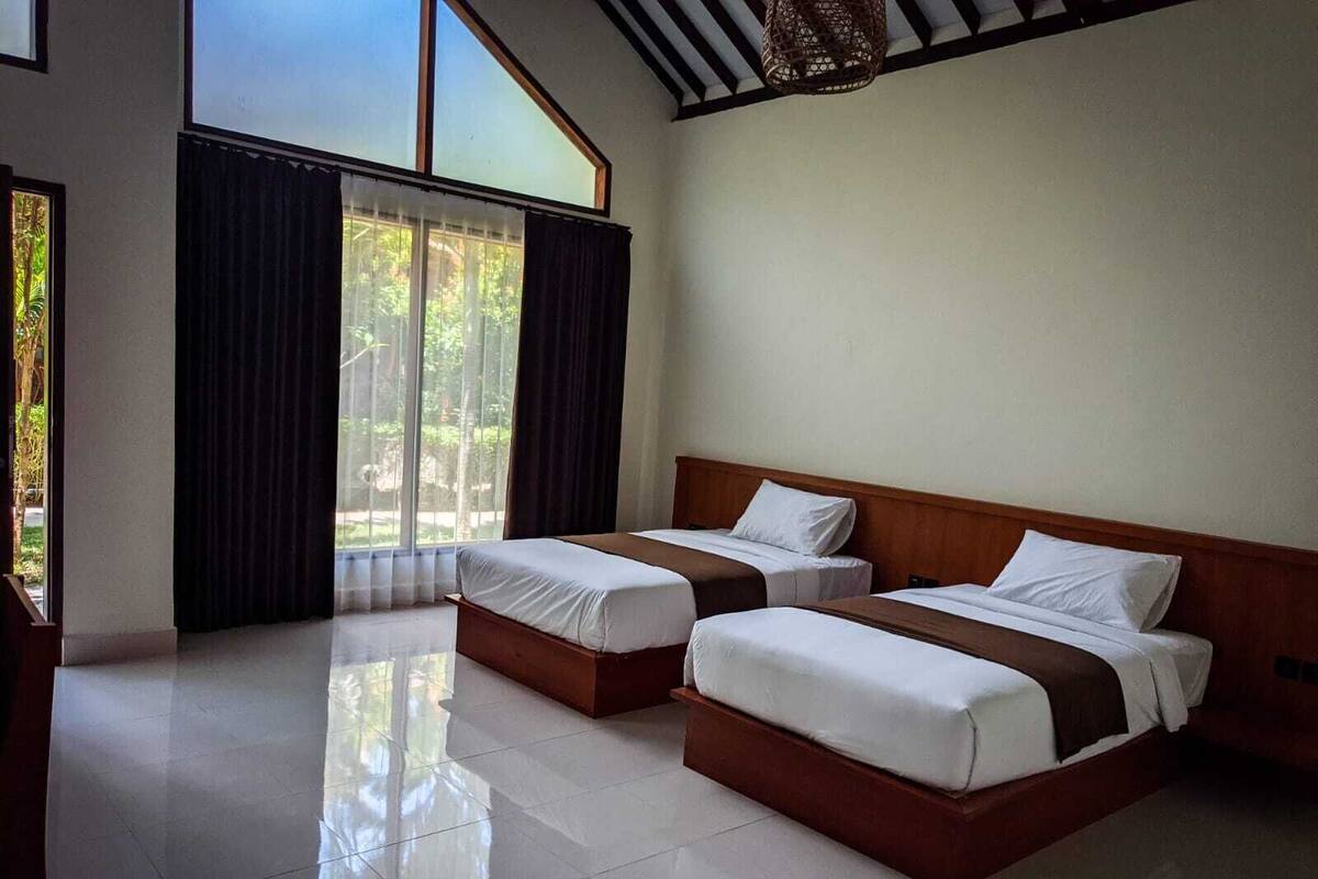 Una habitación de hotel con dos camas, un ventanal con cortinas y suelo de baldosas.