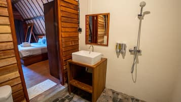 A wooden room with a bed, a wooden cabinet with a sink, a shower, and a mirror on the wall.