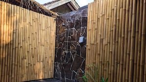 A bamboo fence enclosing a spa area with a stone wall and a shower. - RaCottage Mandalika (Kuta)