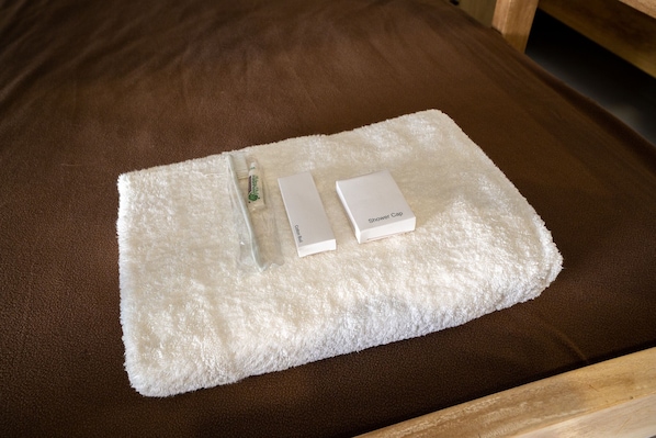 Toalla blanca con gorro de ducha y una botella de loción sobre una cama marrón.