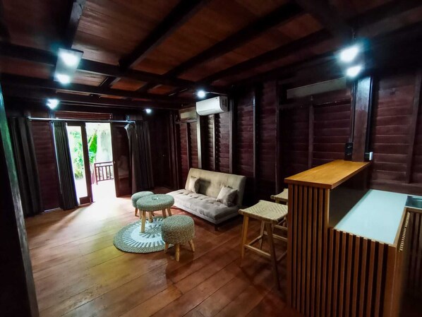 A cozy room with a wooden ceiling, a sofa, two ottomans, a small table, and a bar area.