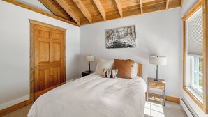 A bedroom with a wooden ceiling, a large bed, two bedside tables with lamps, a painting on the wall, and a window with blinds. - Idyllic Stowe Home and pvt Suite (Stowe)