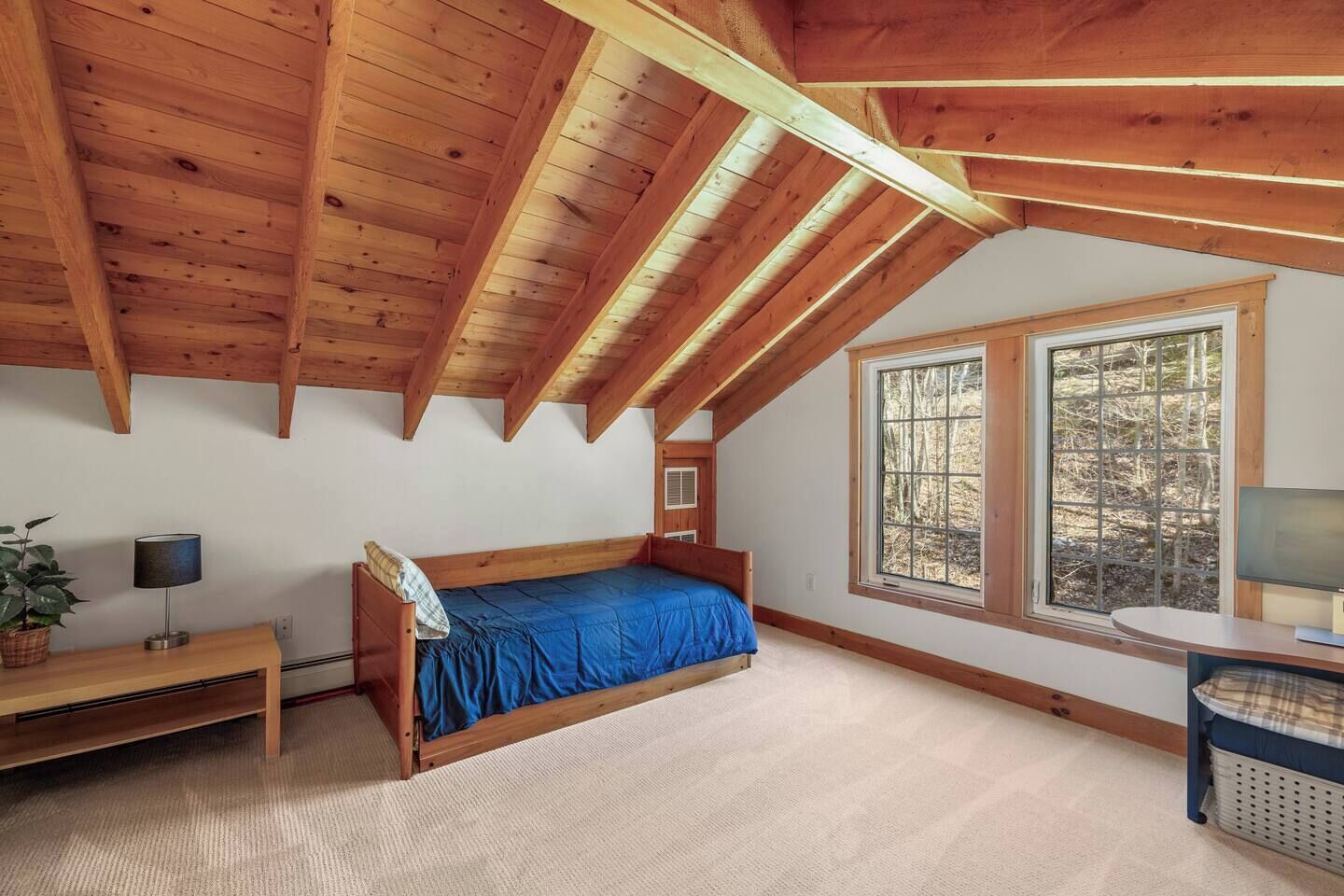 Ein Schlafzimmer mit Holzboden, einem Einzelbett, einem Schreibtisch, einem Stuhl und einem Fenster mit Blick auf Bäume.