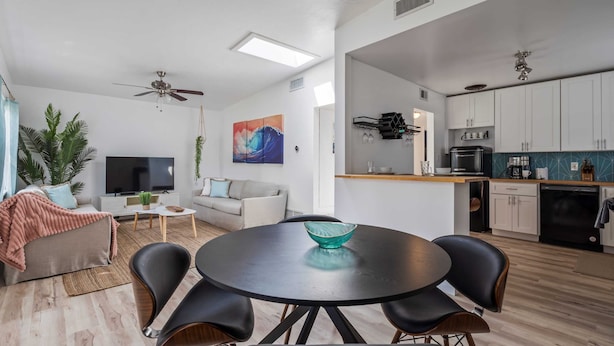 A modern living room with a round dining table, black chairs, a sofa, a TV, and a ceiling fan. - Bay Breeze Bungalow (St. Augustine)