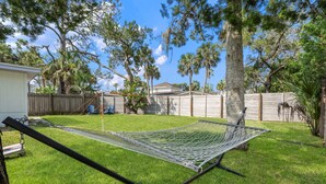 A hammock set up in a backyard with a wooden fence, a white building, and trees. - Bay Breeze Bungalow (St. Augustine)