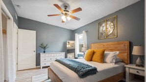 A bedroom with a wooden bed, a ceiling fan, a nightstand, a dresser, and a mirror. - Bay Breeze Bungalow (St. Augustine)