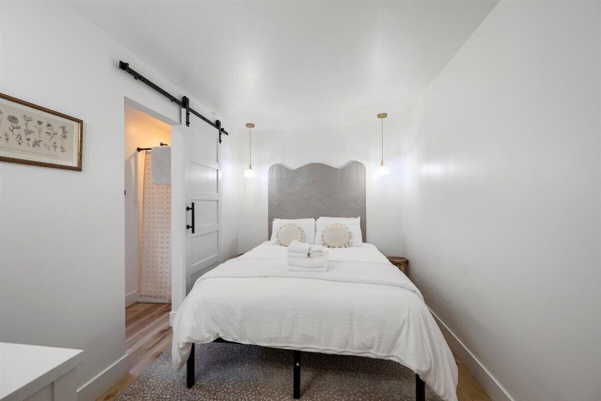 Een slaapkamer met een bed, nachtkastjes, een hoofdeinde en een deur naar een badkamer.