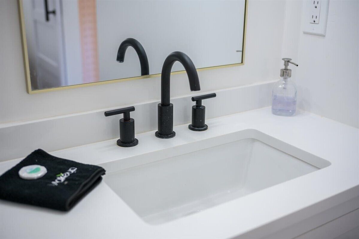 Un baño con lavamanos blanco, grifos negros y dispensador de jabón.