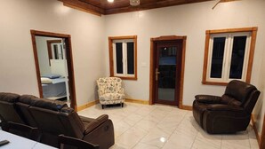 A spacious living room with a marble floor, two leather recliners, a patterned armchair, and a dining table.