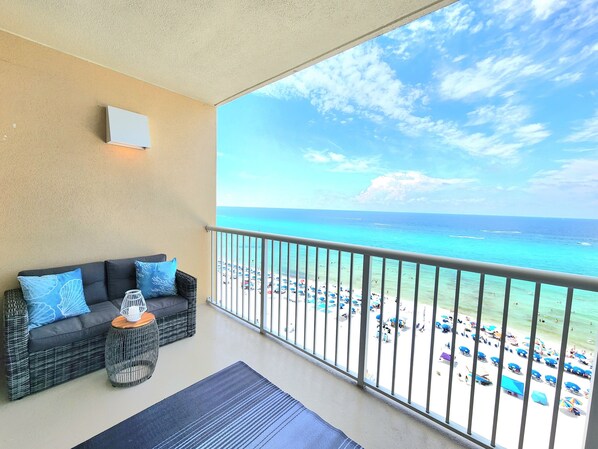A balcony with a view of a beach, a sofa with cushions, and a small table with a decorative item.