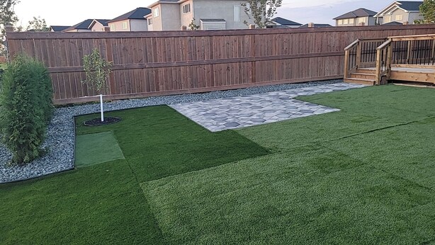 Un jardin avec une pelouse artificielle, une terrasse en pierre et une clôture en bois.