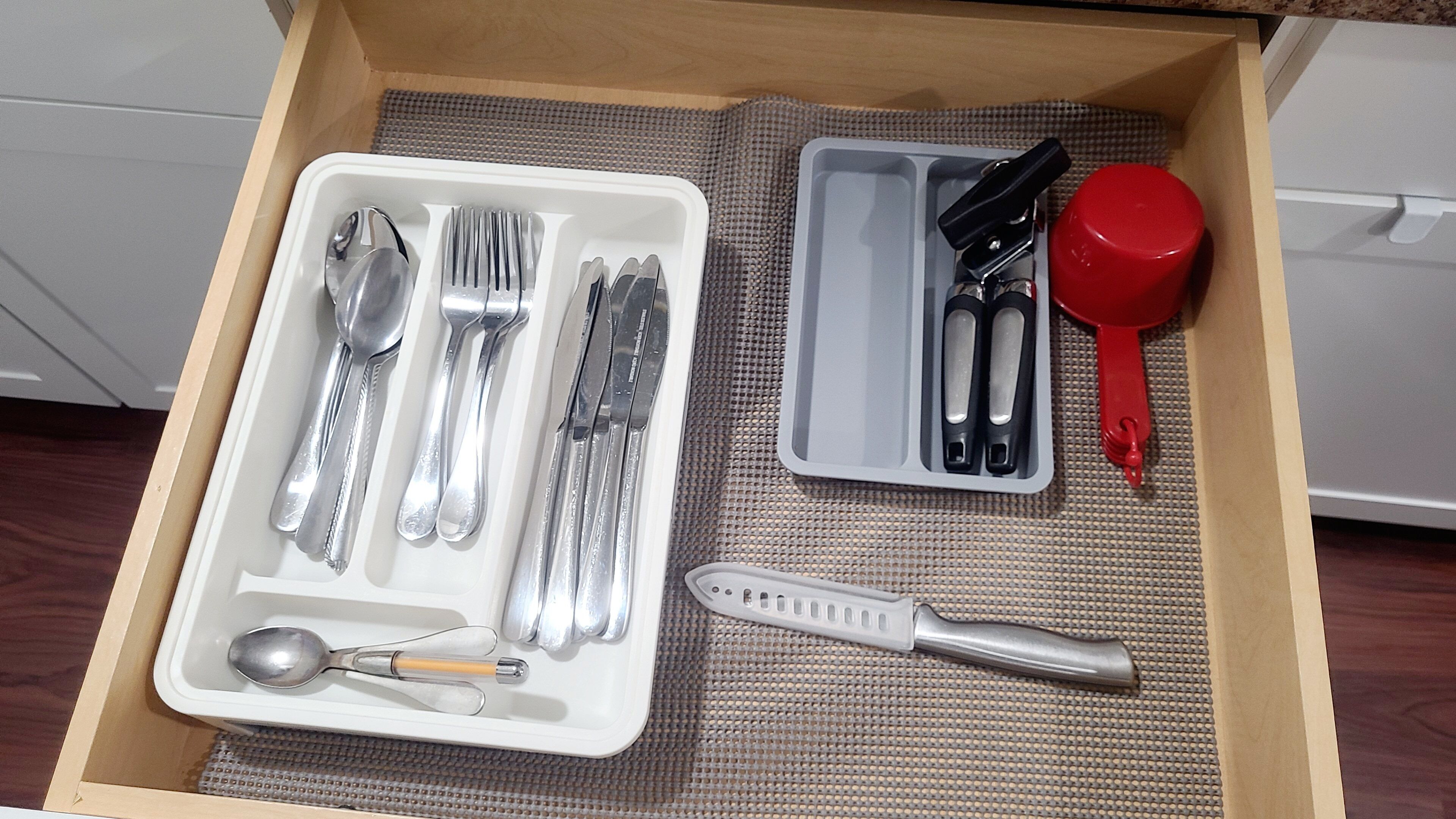 A drawer with a set of silverware, a red measuring cup, and a knife.