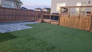 Un jardin avec une pelouse artificielle, un chemin de pierres et une clôture en bois.