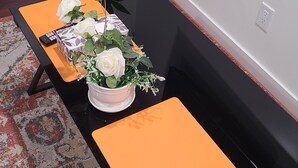 Une pièce avec un canapé noir, une petite table sur laquelle est posé un vase de fleurs blanches, une plante en pot et un tapis à motifs.