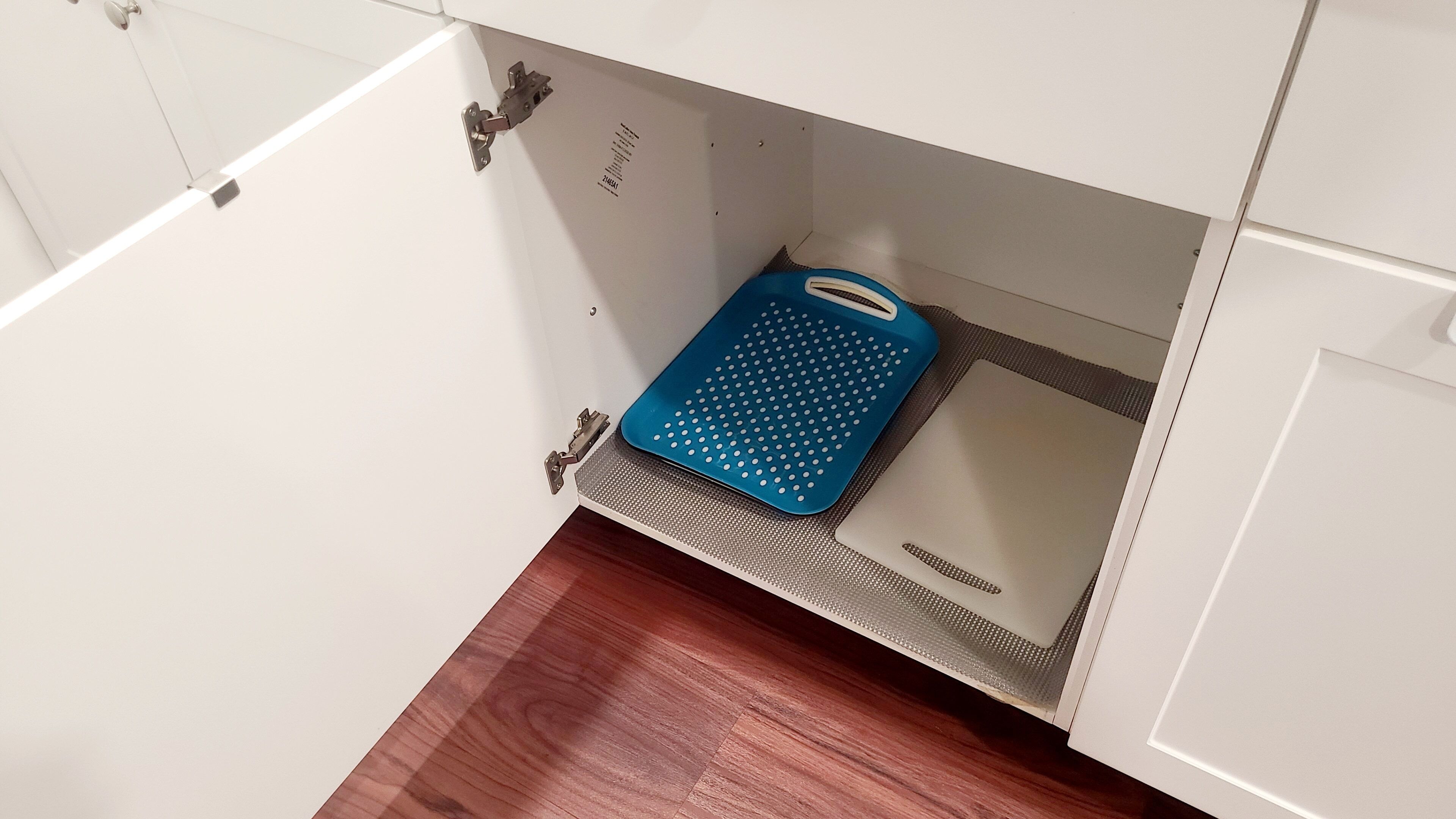 A bathroom with a white cabinet, a blue mat, and a wooden floor.
