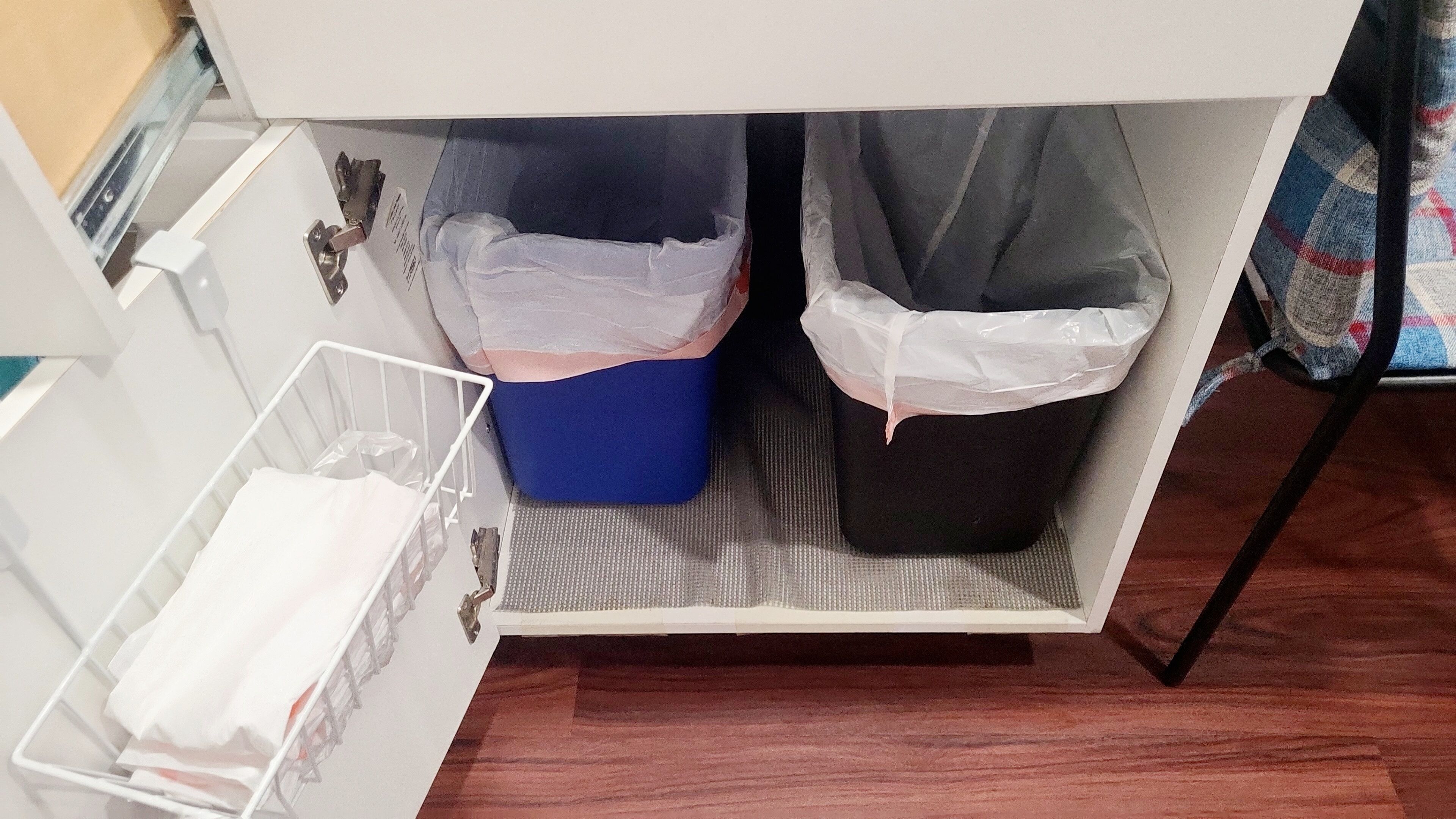 Un meuble de rangement blanc, doté de deux compartiments, un bleu et un noir, contenant des sacs poubelles blancs.