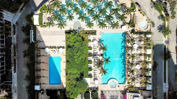 Vue aérienne d’un complexe hôtelier doté de deux grandes piscines, de palmiers et d’espaces de détente.