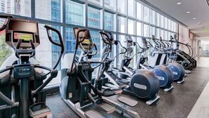 Une rangée de vélos d’appartement et d’appareils de musculation elliptique dans une salle de sport dotée de grandes fenêtres.