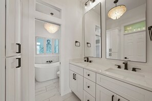 A modern bathroom with a freestanding bathtub, a large mirror, and a chandelier. - The Hummingbird - Lakefront Vacation Home with Private Pool & Water Views (Destin)