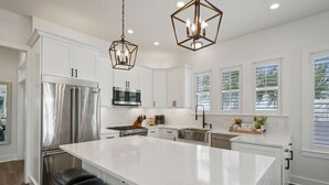 Una cocina moderna con armarios blancos, electrodomésticos de acero inoxidable, una isla grande e iluminación colgante.