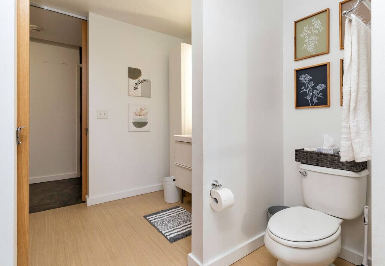 A bathroom with a toilet, a sink, a shower curtain, and framed wall art.
