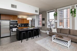 A modern kitchen with a central island, bar stools, a dining area with a sofa, and large windows with city views.