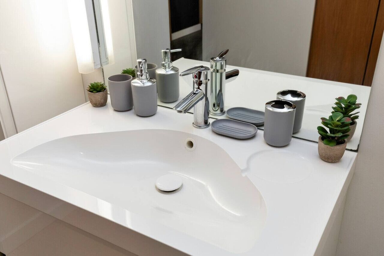 A modern bathroom with a white sink, chrome faucet, and various toiletries.