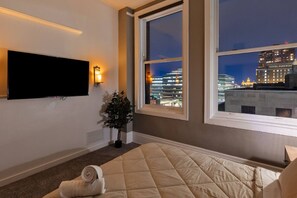 A hotel room with a large window, a flat-screen TV, a bed, and a small potted plant.